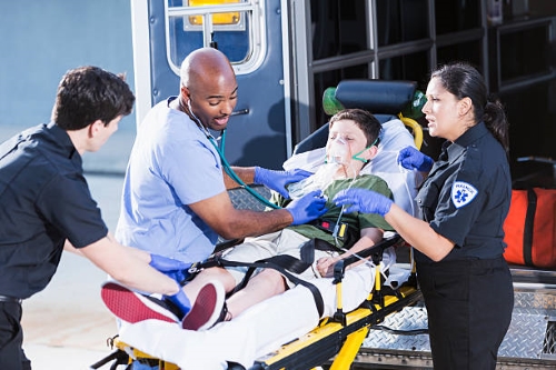 EMS personnel work with a patient on a gurney behind an ambulance