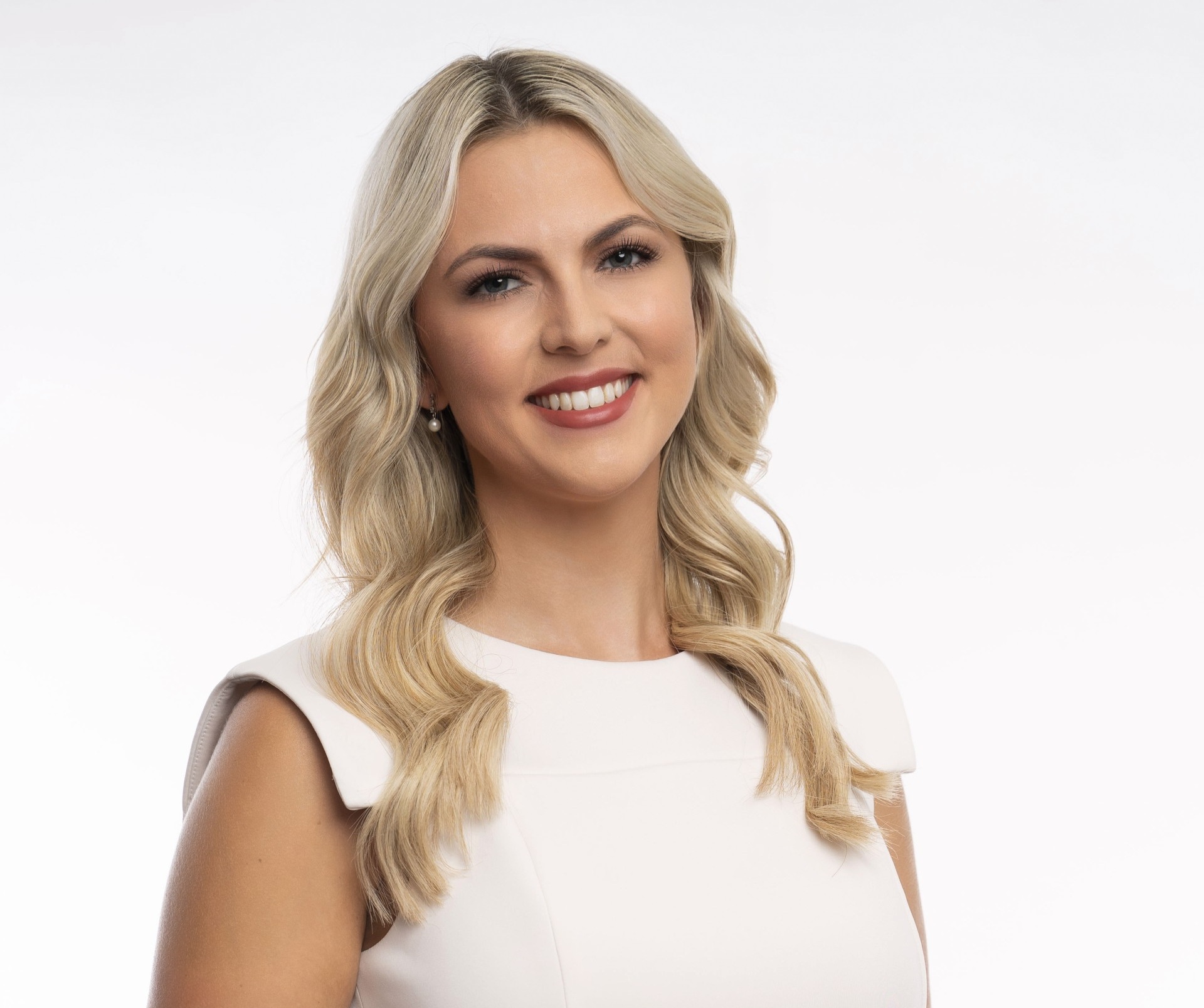 Chelsea Helms smiles in a headshot photo of her in a white dress against a blank backdrop