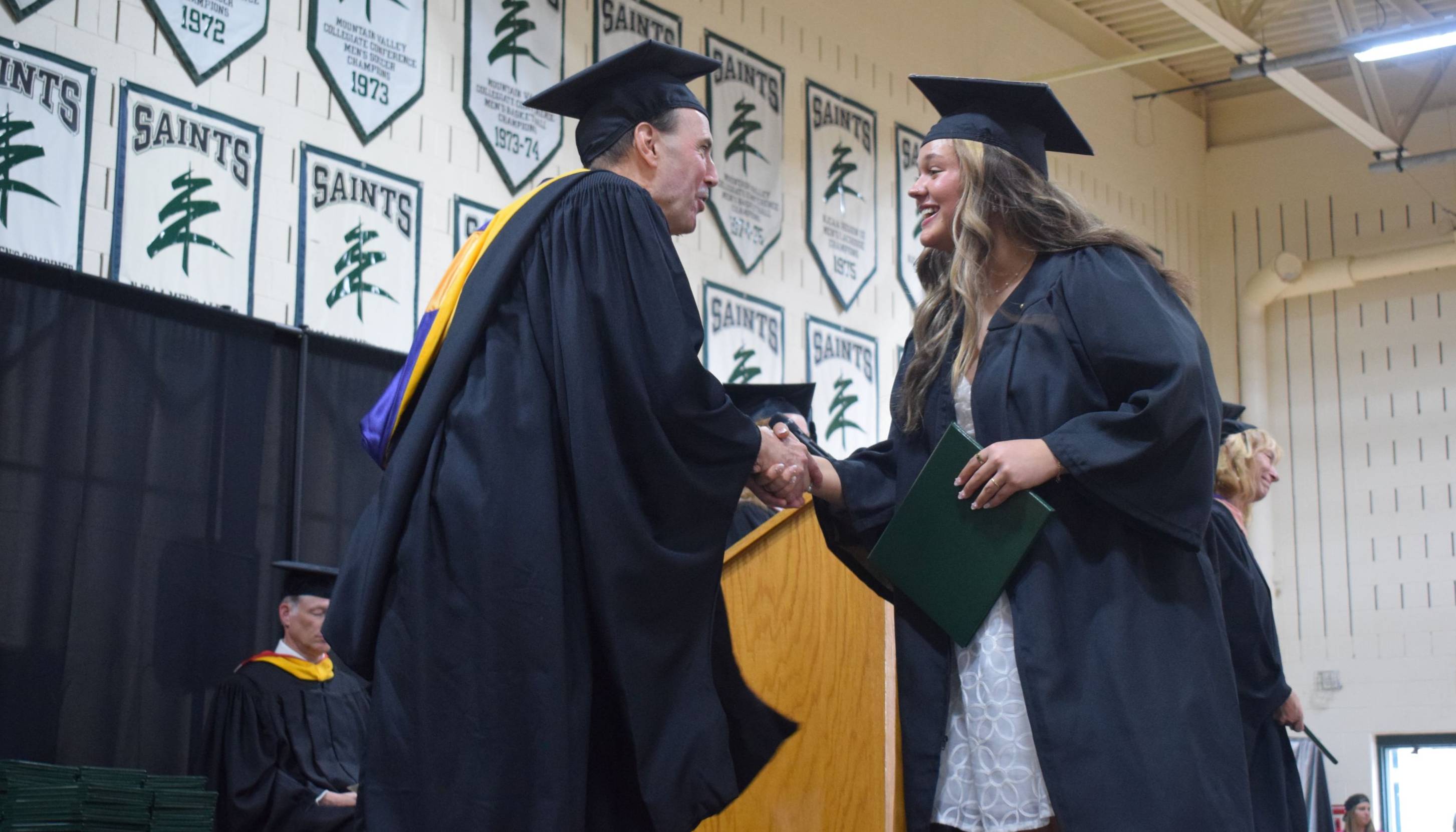 A graduate shakes hands with the college president as she crosses the stage