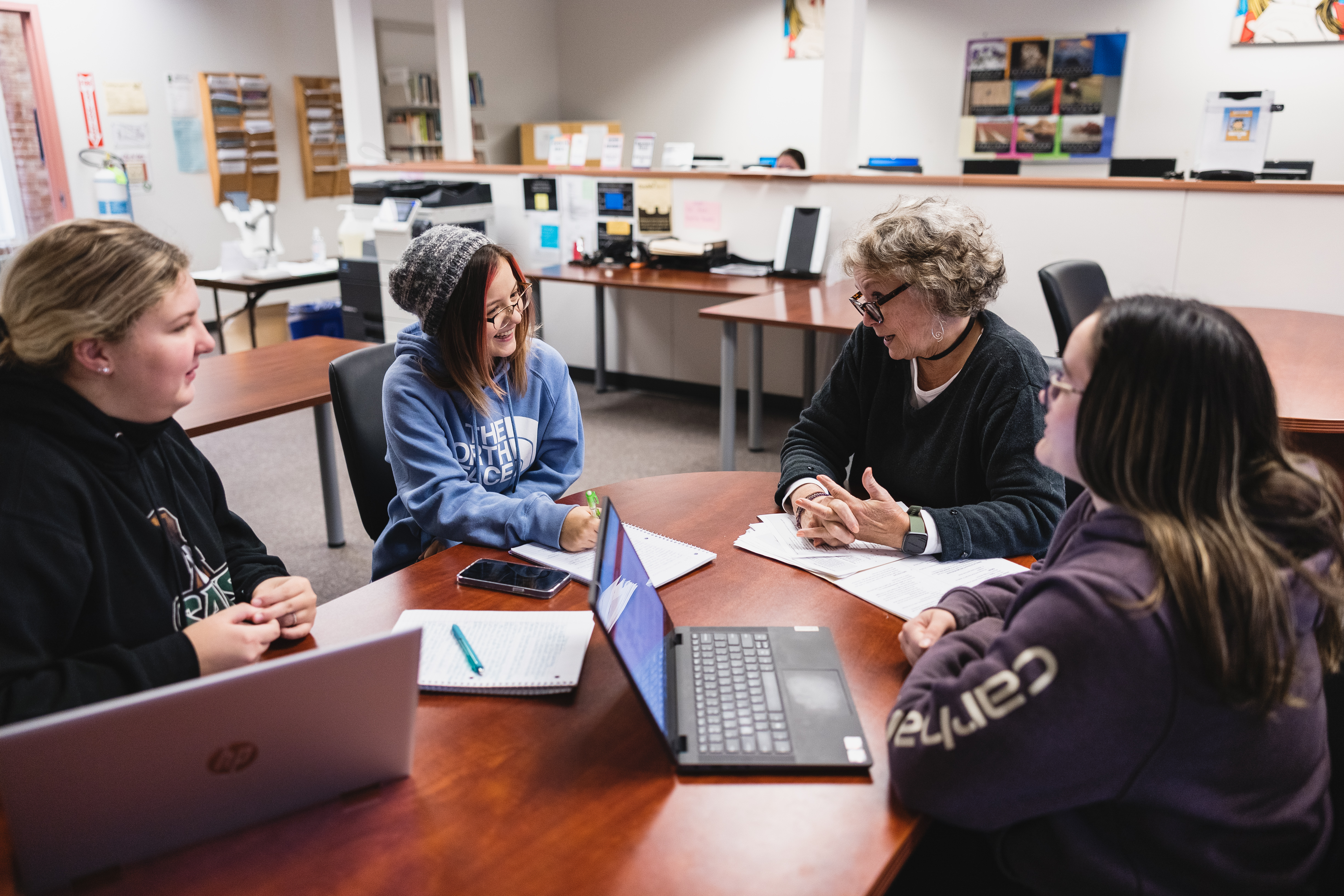 An instructor works with a small group of students at a table in a classroom.
