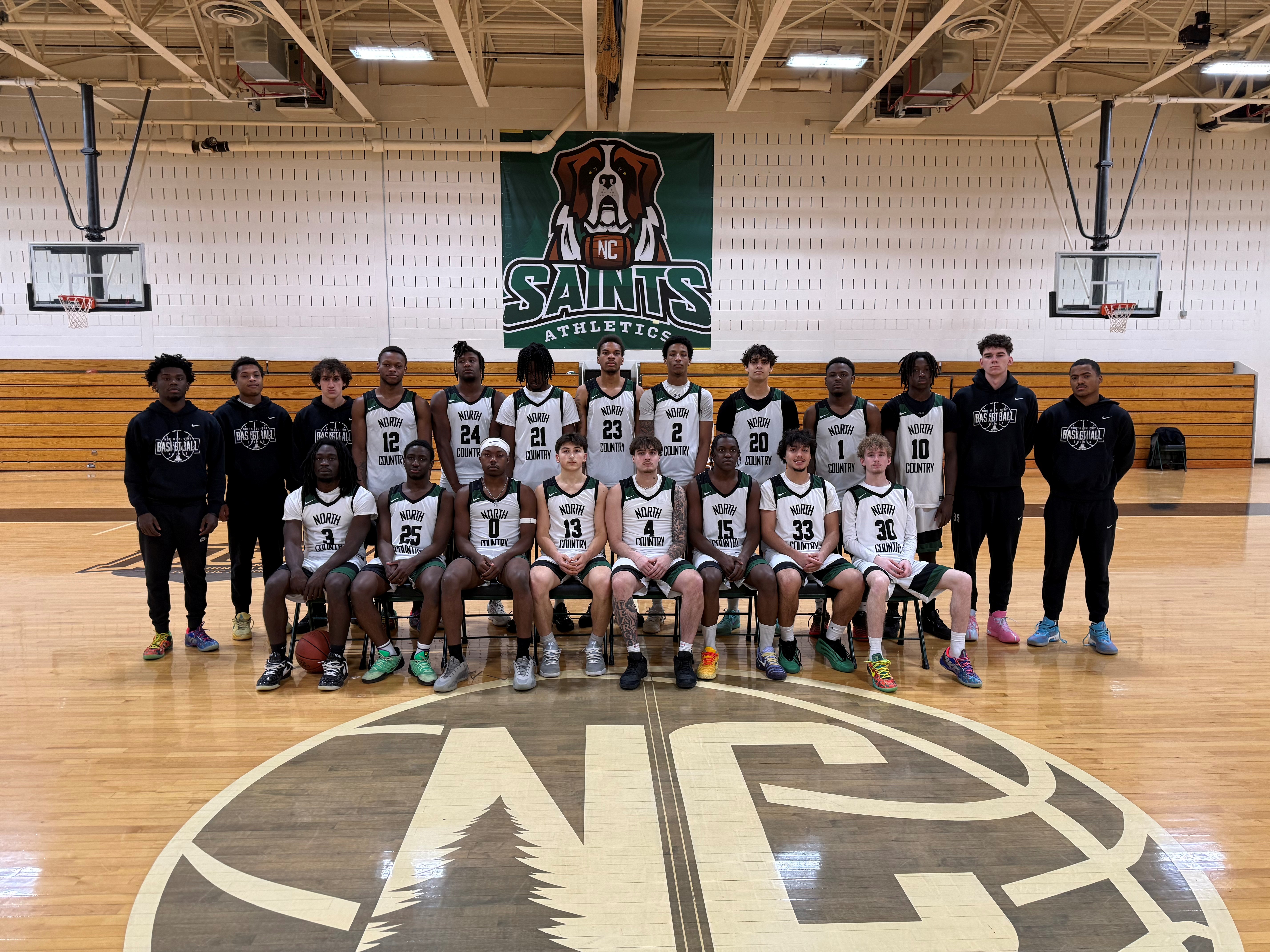 A basketball team stands shoulder to shoulder for a team picture in the college gym.