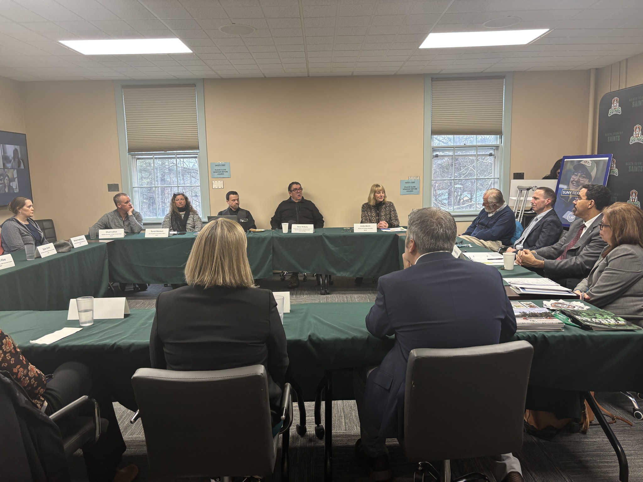 A group of people are seated around a series of tables in a college classroom