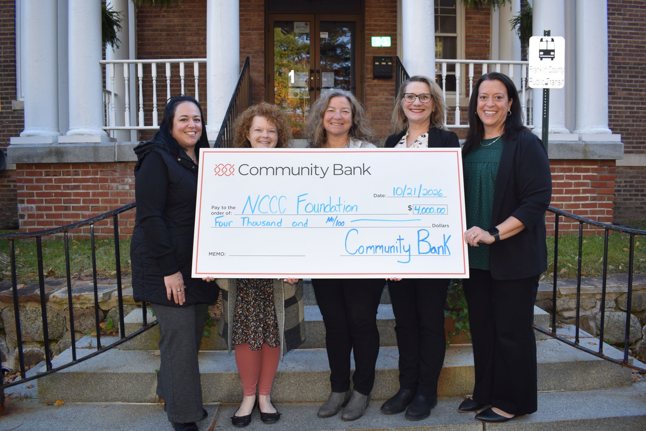 A group of people stand behind an oversized check outside a college building