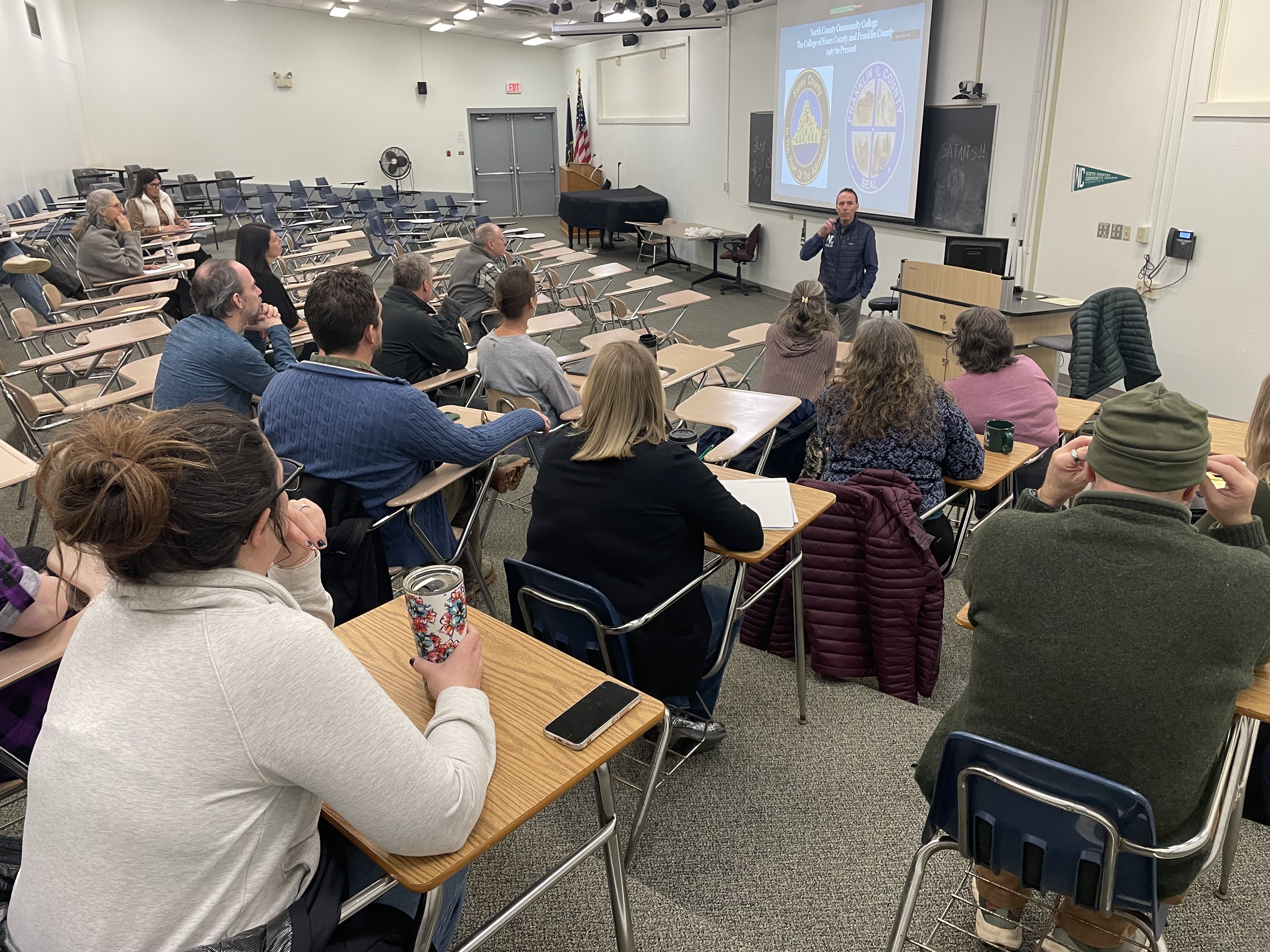 College employees sit in a lecture hall as they listen to the college president.