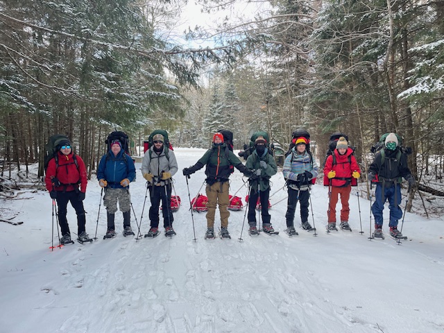 Students in North Country's Wilderness Rec program, dressed in winter gear and wearing snowshoes, stand together and face the camera.
