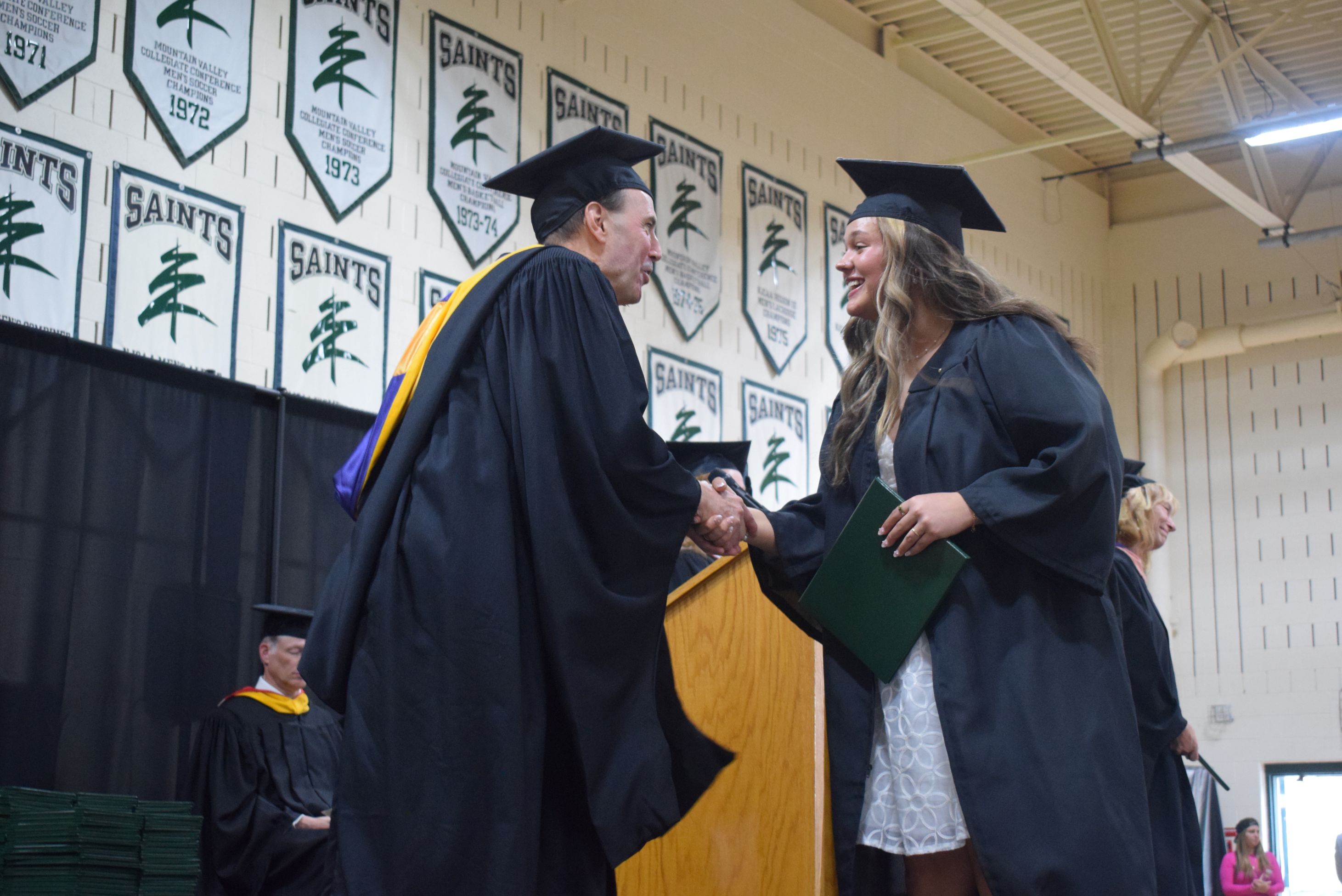 A student shakes hands with the college president on stage