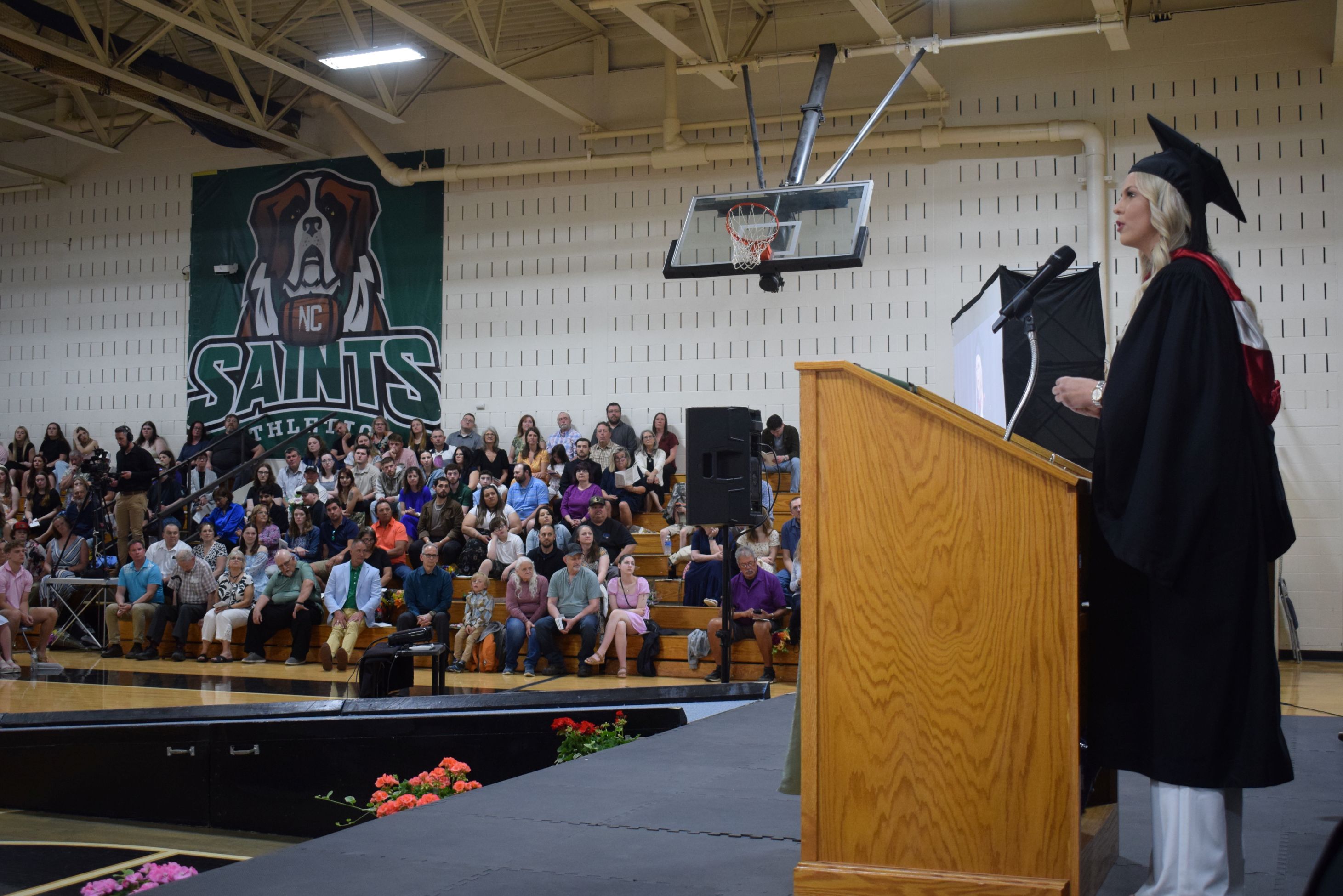 A speaker stands behind a podium speaking to the audience in a college gym