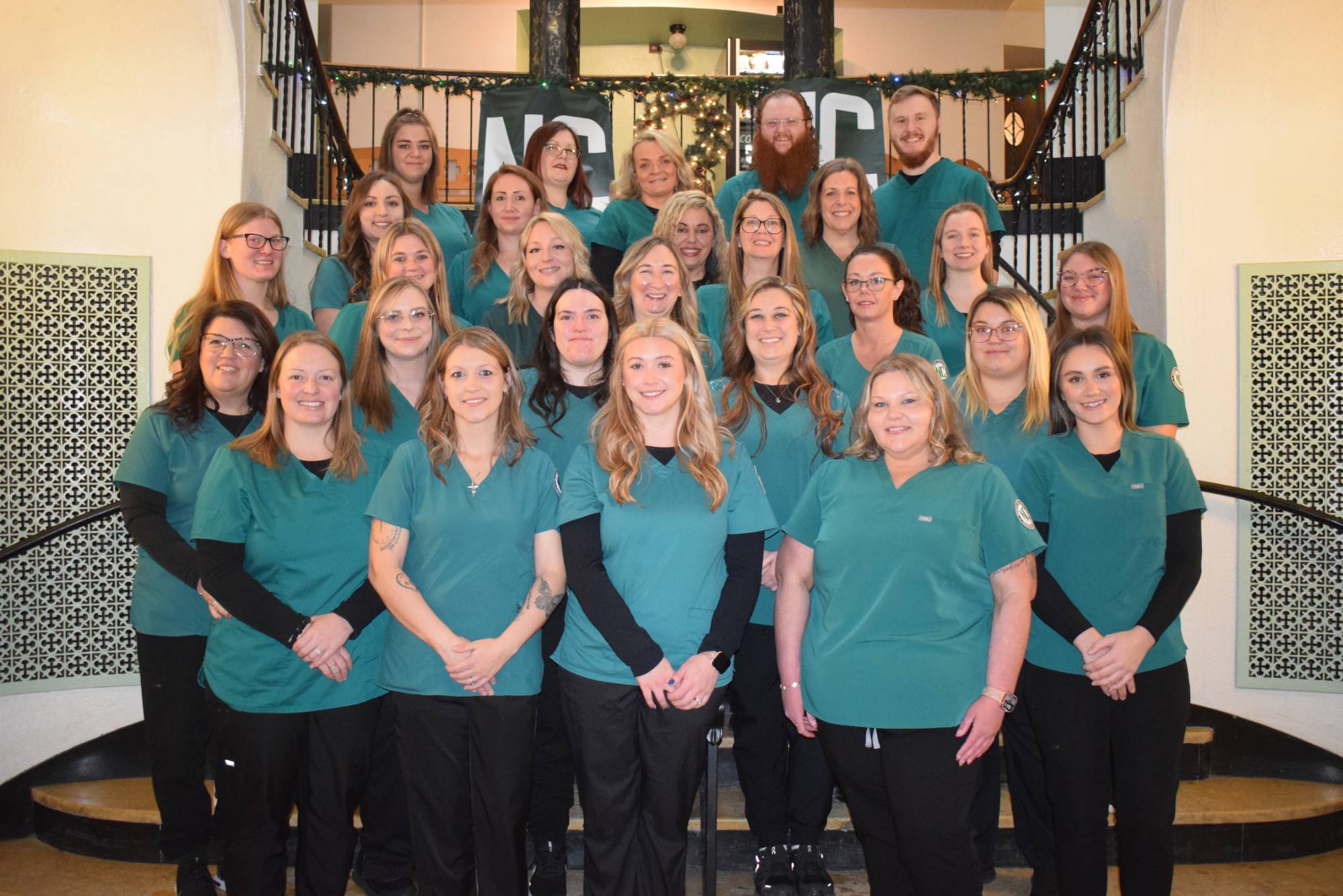 Nursing students in uniform stand as a group on the steps of a stairwell for a group photo