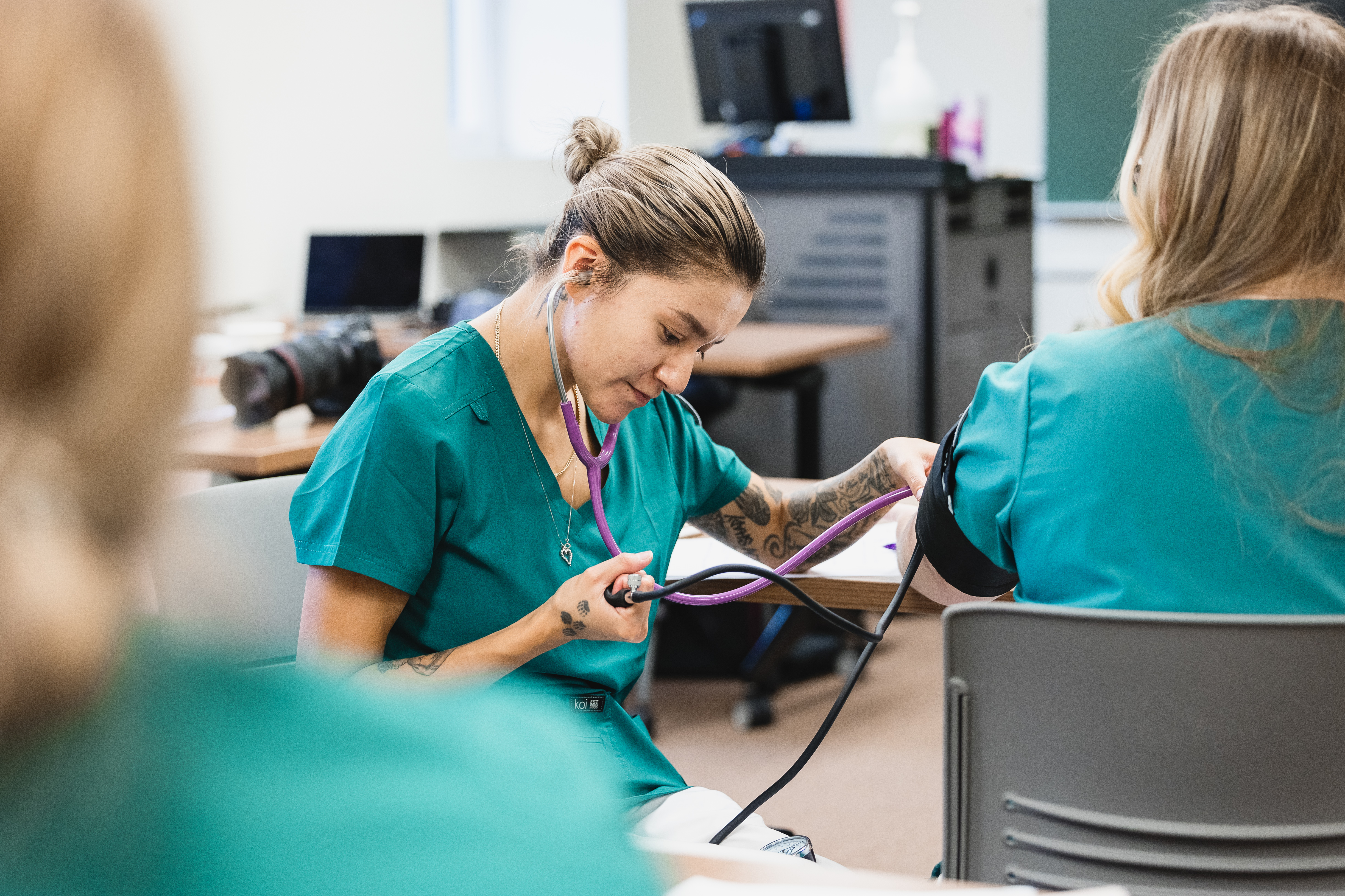 Nursing student takes another student's blood pressure in a classroom